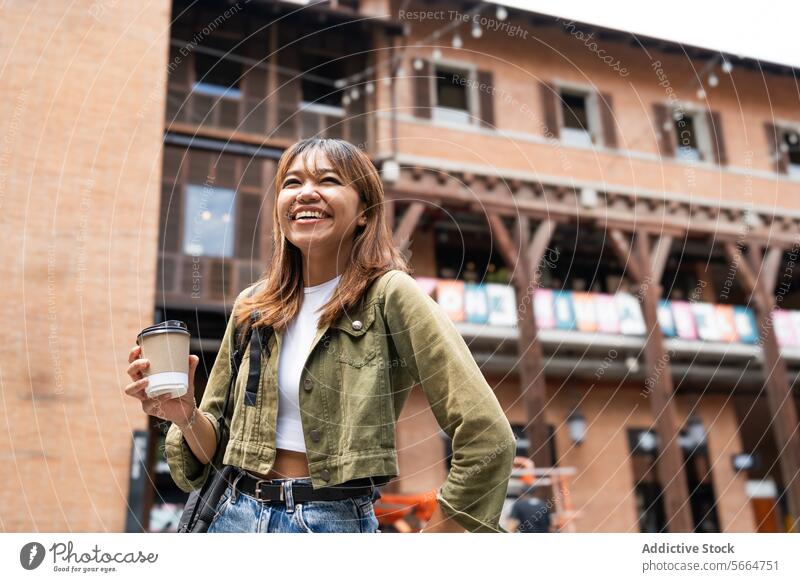 Fröhliche asiatische Frau mit Rucksack und Kaffeetasse, die im Freien spazieren geht und das flexible Leben der Telearbeit in Chiang Mai, Thailand, vorstellt