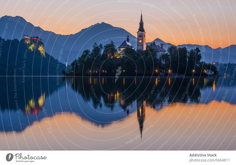 Die Sonne geht über dem Bleder See unter und wirft ein warmes Licht auf die Wallfahrtskirche Mariä Himmelfahrt und die Burg von Bled. Sonnenuntergang lake bled