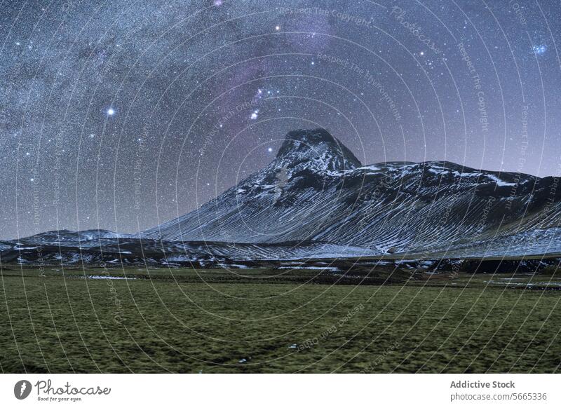 Sternenübersäter Nachthimmel mit der Milchstraße über einem schneebedeckten Berg und einem grasbewachsenen Feld im isländischen Winter Island Milchstrasse