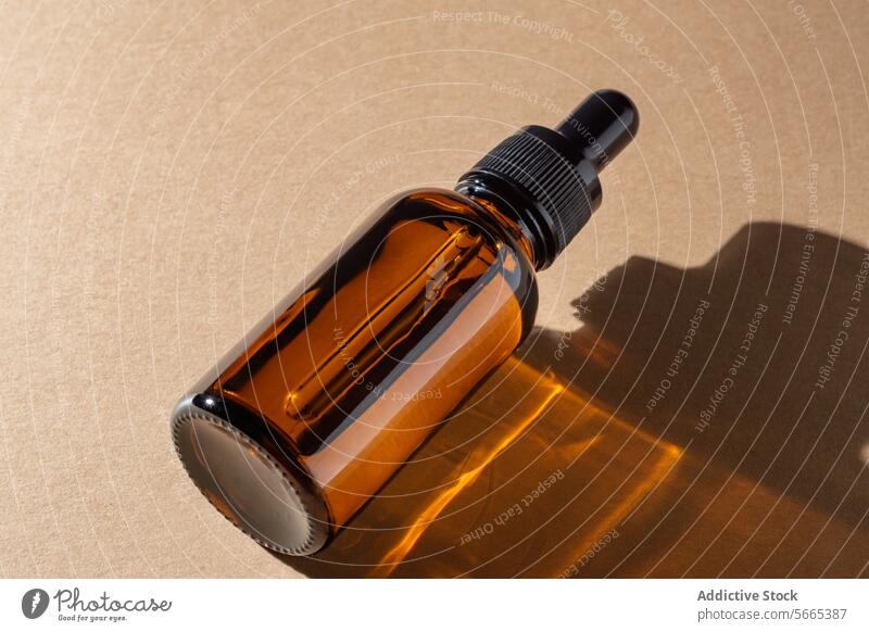 Braunglas-Tropfflasche, die einen warmen goldenen Schatten auf eine beigefarbene Oberfläche wirft, mit einer minimalistischen Ausstrahlung Flasche Tropfer