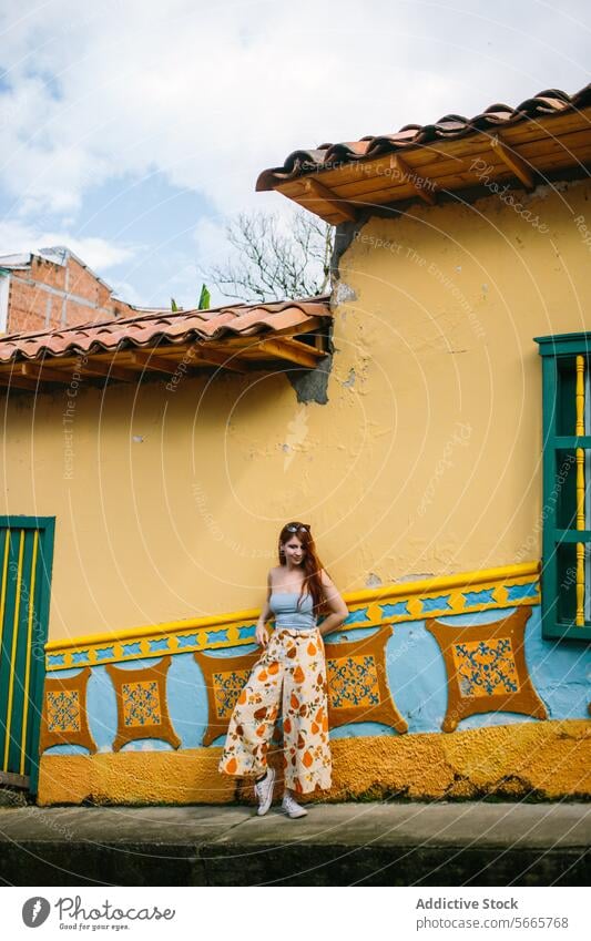 Modische Frau posiert vor einem bunten Gebäude in Guatapé Mode Stil farbenfroh traditionell Wand pulsierend jung stylisch Kleidung Lehnen Design Element gelb