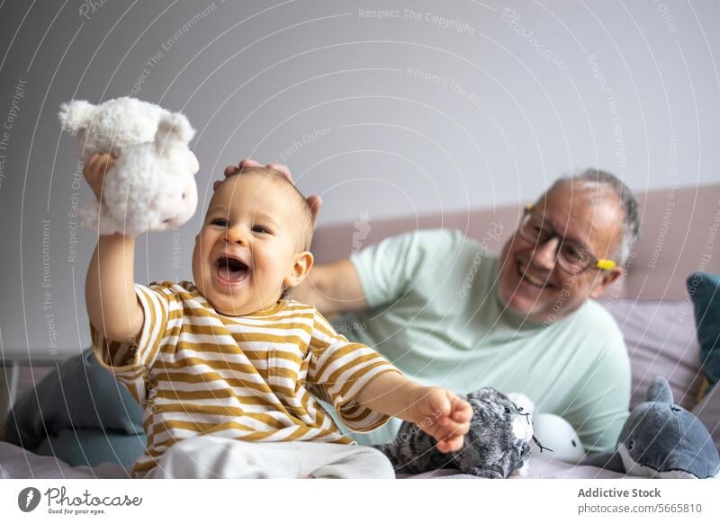 Großvater und Enkelkind genießen spielerische Zeit miteinander Baby spielen Freude Lächeln Bett Plüschtier Familie Fröhlichkeit Bonden