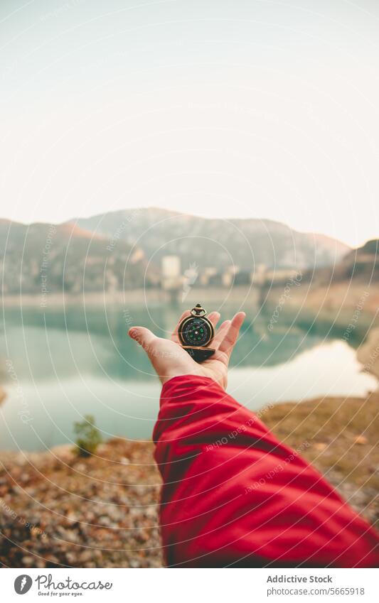 Anonyme Hand, die einen Kompass hält, mit einem malerischen See und Bergen im Hintergrund, die Führung und Erforschung symbolisieren Berge u. Gebirge Anleitung