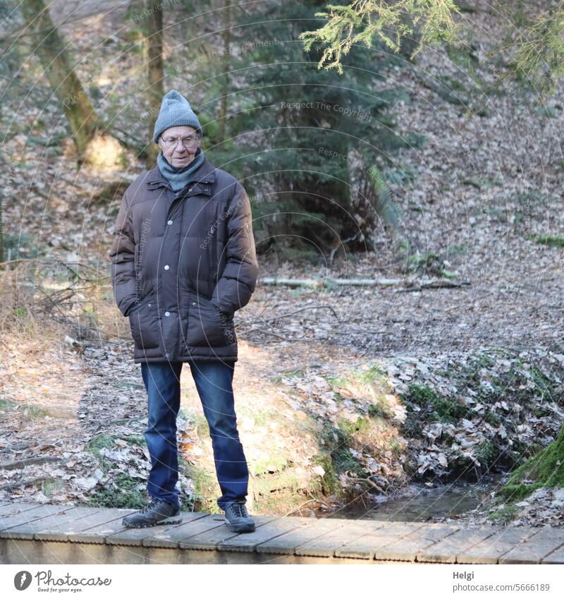 Senior steht auf einem Steg im Wald Mensch Mann Erwachsener stehen Bach Winter Winterbekleidung Sonnenlicht schauen Natur Außenaufnahme Farbfoto Umwelt maskulin