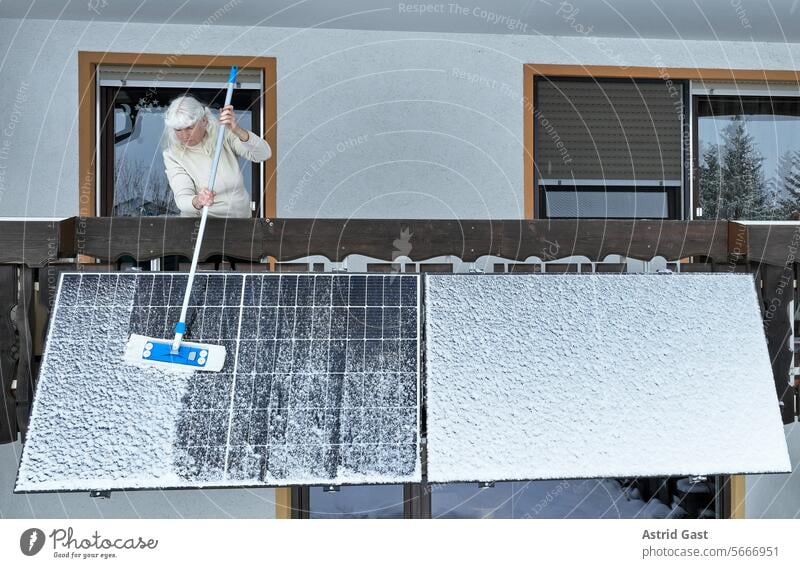 Eine Frau befreit im Winter ein Balkonkraftwerk vom Schnee balkonkraftwerk solar stromerzeugung Schafe kehren säubern pflegen freiräumen stromerzeugen Haus