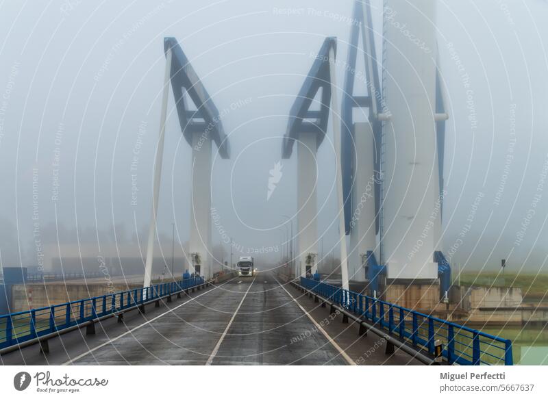 Lastwagenfahrt auf der Zugbrücke der Schleuse von Sevilla an einem nebligen Tag. Schloss Brücke Straße Fluss Gegengewicht Umlauf Verkehr Nebel Anhänger