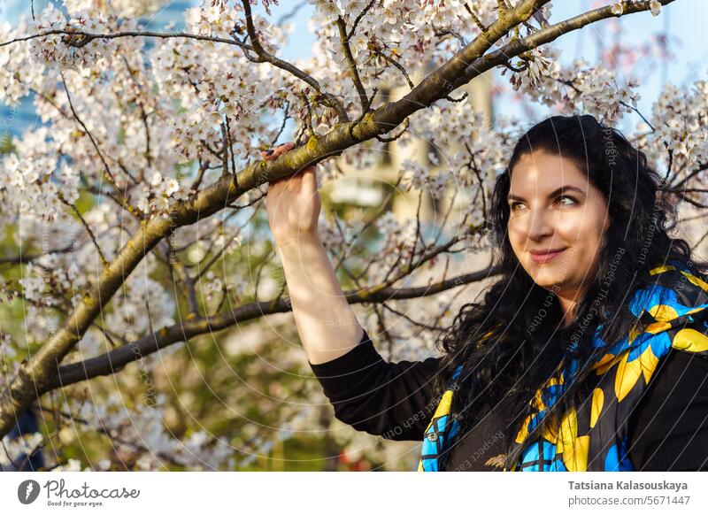 Junge Frau auf dem Hintergrund der blühenden Kirschbäume im Stadtpark jung Überstrahlung Kirsche Bäume Großstadt Frühling urban Blüte Baum im Freien Natur