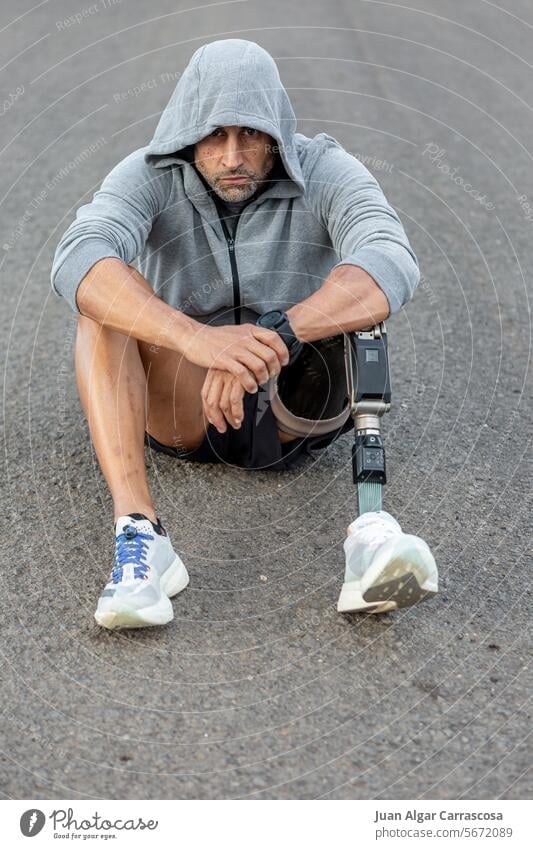 Behinderter männlicher Sportler auf asphaltierter Straße sitzend Training Handicap Amputierte Asphalt Prothesen Fitness unglücklich Pause Lebensmitte reif