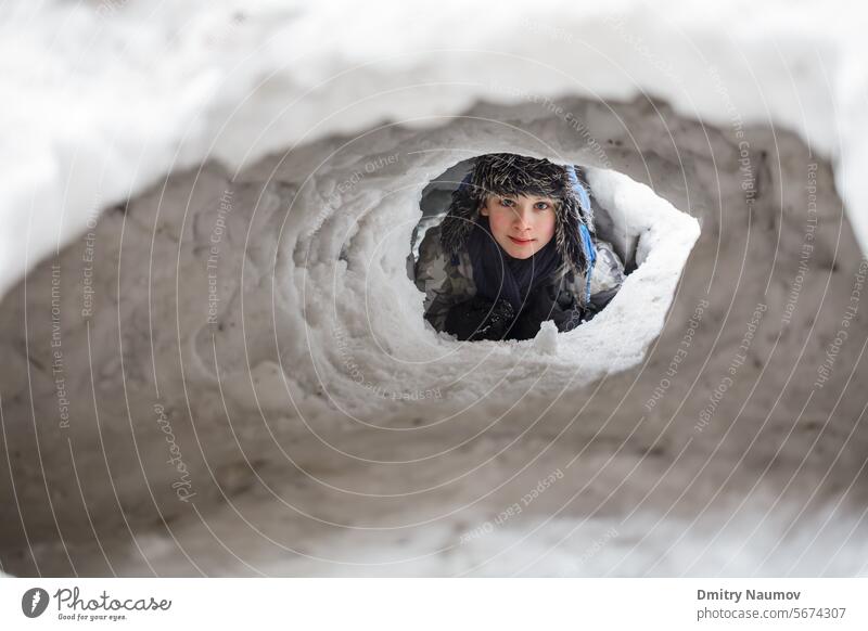 Kleiner Junge versteckt sich in einer selbstgebauten Schneehöhle 12-13 Jahre Iglu in die Kamera schauen warme Kleidung Kaukasier Höhle Kind kalt niedlich tief