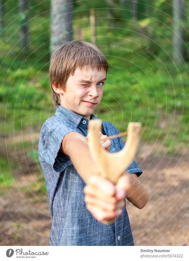 Junge zielt mit Holzschleuder im Freien Genauigkeit Aktivität zielen Arme schlecht Bohnenschütze Verhalten Gören Kaukasier Kind Gefahr Gesicht Flip Spaß Spiel
