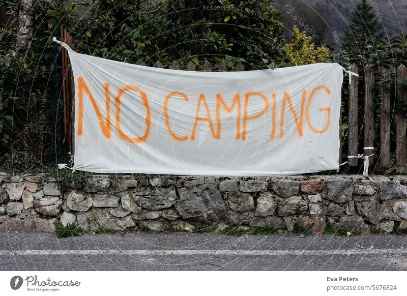 Eine Fahne auf der "No Camping" steht über einer kleinen Mauer vor einem Gartenzaun no camping Wohnwagen Natur Erholung Campingplatz Tourismus Sommerurlaub