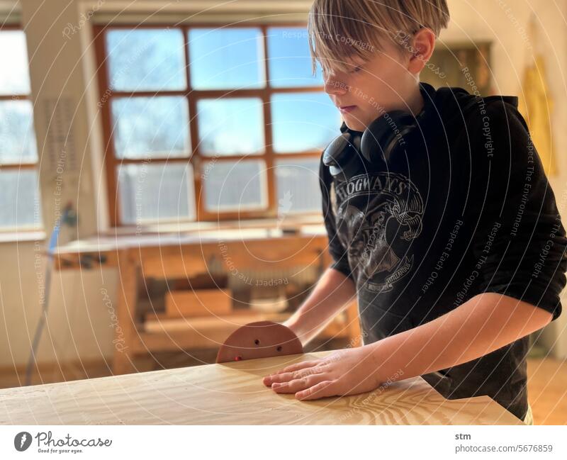 Junge in der Werkstatt Tischlerei Schleifmaschine Exzenterschleifer Handschleifgerät Handwerk Handwerk lernen Sorgfalt Schleifen Holzbearbeitung Kind