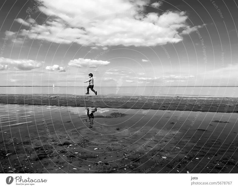 Junge rennt am Meer entlang spieglung Norddeutschland maritim Ostsee Strand ufer verspielt rennen springen verspieltheit Spielen Freude Leichtigkeit Kindheit