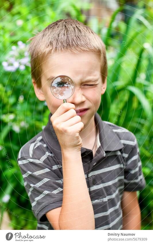 Junger Junge schaut durch eine Handlupe im Freien 7 Jahre Kaukasier Kind Kindheit zugeklappt entdecken Bildung Umwelt Erkundung Auge Garten Glas Halt Lernen