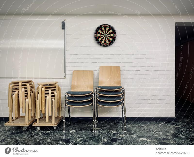 Stühle und Hocker vor einer weißen Wand mit Whiteboard und Dartscheibe Stapel Sitzgelegenheit Seminar Seminarraum Stuhl Menschenleer Steinfliesen