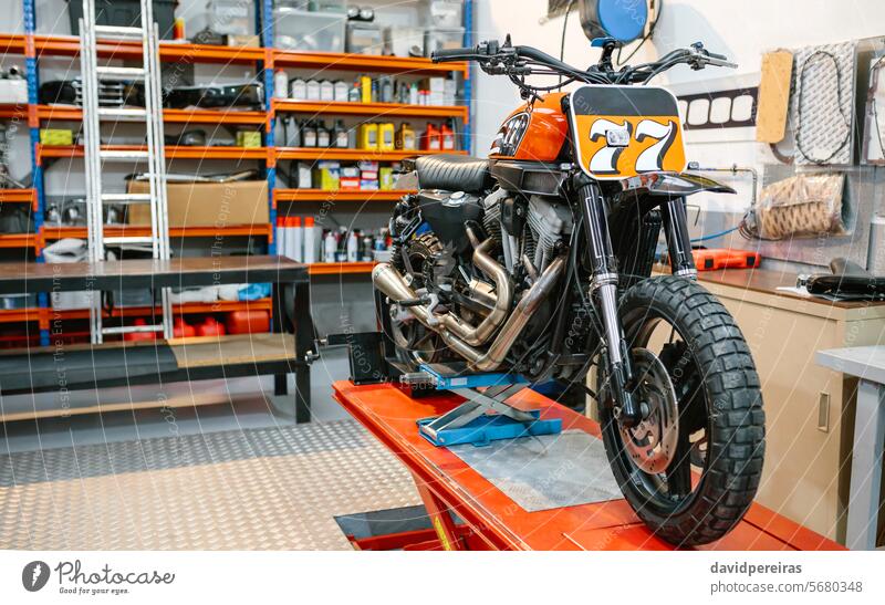 Schwarzes und rotes Custom-Motorrad auf der Plattform, bereit, eine leere Werkstatt zu überprüfen benutzerdefiniert Podest altehrwürdig retro Garage Fabrik
