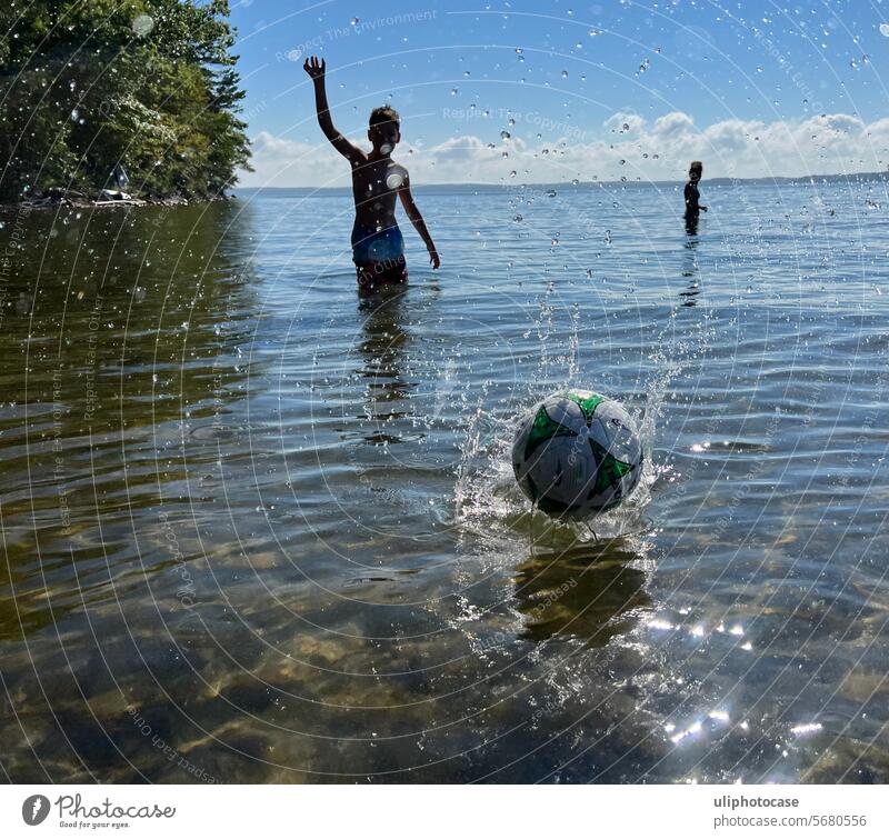 Junge im Gegenlicht, der einen Ball in Richtung  Fotograf auf das Wasser wirft Gegenlicht am Wasser Ballspiel Wasserball Silouhetten