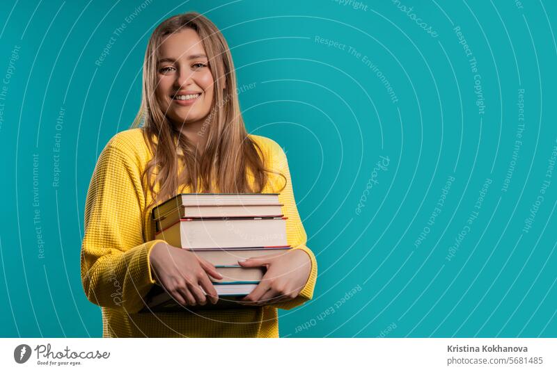 Glückliche Studentin mit Bücherstapel aus der Bibliothek, blauer Hintergrund. Kopieren Raum Amerikaner Waffen attraktiv schön Buch lässig clever Hochschule