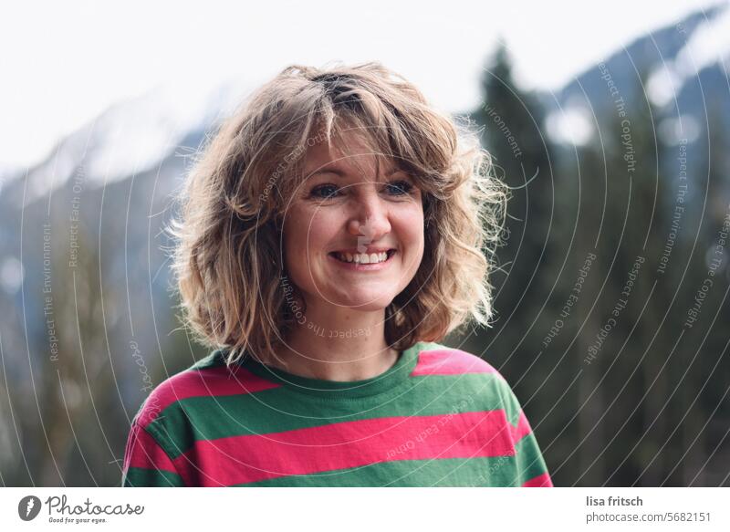 FRAU - LÄCHELN - ZWISCHEN BÄUMEN UND BERGEN Frau 30 - 40 Jahre blond Locken gestreift Winter Berge u. Gebirge Bäume Lächeln freudig positiv Erwachsene Farbfoto