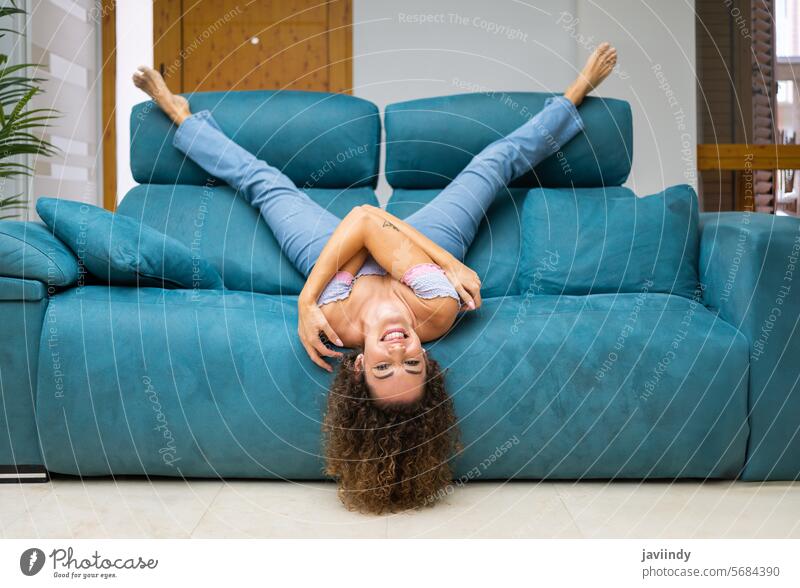 Fröhliche Frau liegt kopfüber auf dem Sofa zu Hause auf den Kopf gestellt Lügen heimwärts Spaß haben Glück Wohnzimmer Lächeln sich[Akk] entspannen Lachen