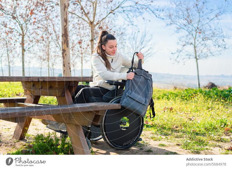 Eine junge Frau im Rollstuhl sortiert ihren Rucksack an einem Tisch im Park organisierend im Freien Freizeitkleidung Sitzen tagsüber Zugänglichkeit