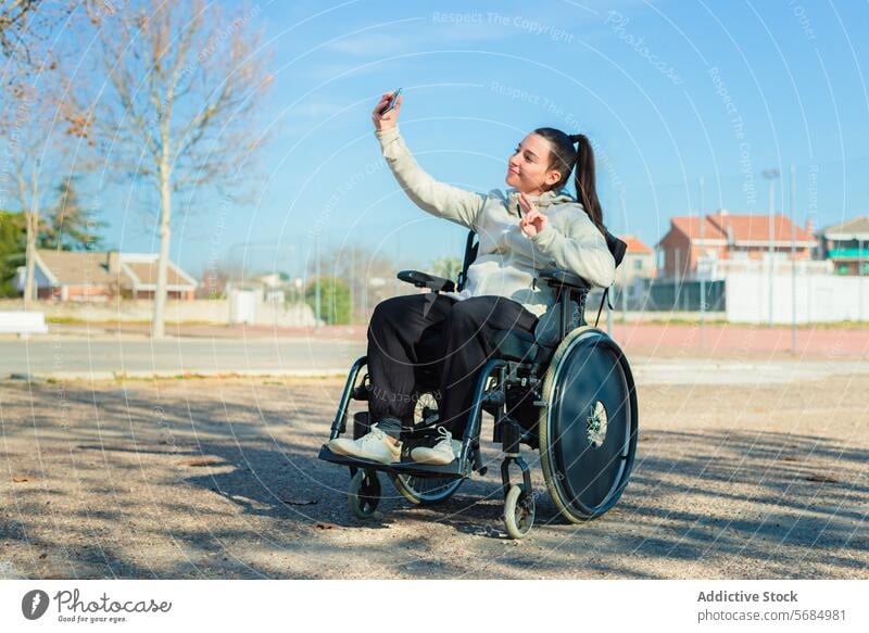 Eine junge glückliche Frau im Rollstuhl macht ein Selfie mit ihrem Smartphone im Park im Freien Fotografie Freizeitkleidung Sitzen tagsüber