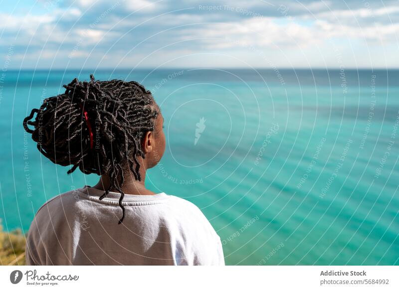 Anonyme afroamerikanische Frau, die während einer Solo-Reise friedlich auf das türkisfarbene Meer blickt MEER ruhig beschaulich nachdenklich Afroamerikaner