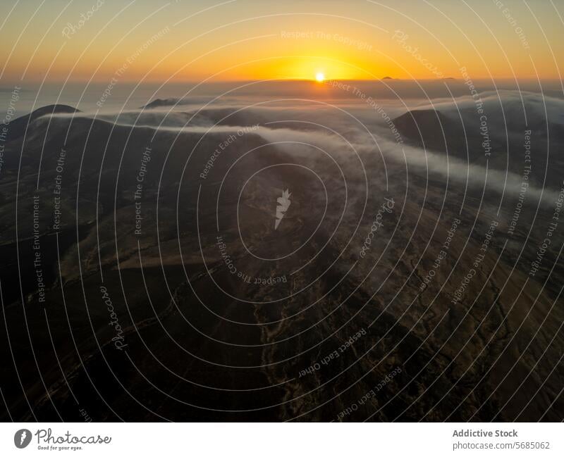Die Sonne erhebt sich über den Horizont und wirft einen warmen Schein über die nebligen Berge Fuerteventuras. Sonnenaufgang Nebel Berge u. Gebirge glühen