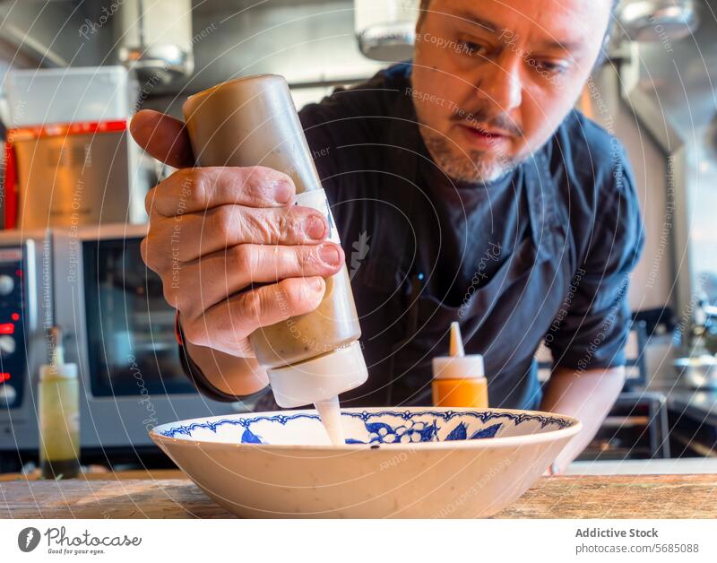 Konzentrierter Koch, der Sahne in den Keramikteller gibt Mann Küchenchef Bestandteil Spender Konzentration Restaurant Teller Geschirr Fokus Teig vorbereiten