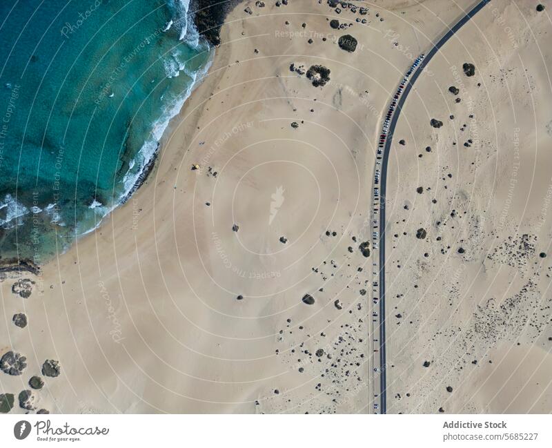 Luftaufnahme einer einzigen kurvenreichen Straße, die sich durch die weitläufigen Dünen von Corralejo schlängelt, während der azurblaue Ozean sanft an die Küste von Fuerteventura spült