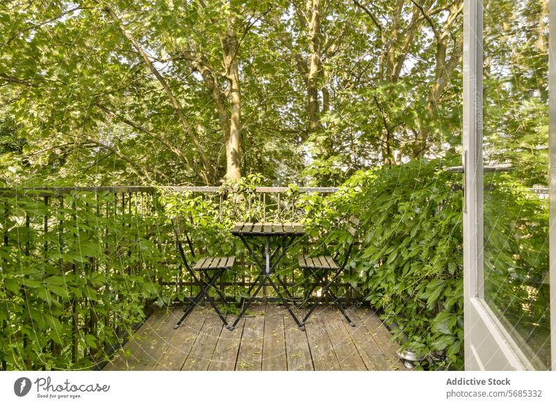 Gemütlicher Balkon, umgeben von üppigem Grün Tisch Stuhl Pflanze Baum urban Flucht Gelassenheit ruhig schwarz Metall im Freien Möbel Schiffsdeck üppig (Wuchs)