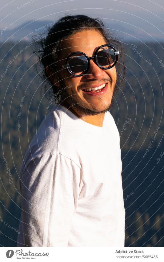 Glücklicher junger Mann am Berghang stehend Natur positiv Zahnfarbenes Lächeln Vollbart lässig Stoff Sonnenbrille anhaben reisen Ausflug genießen männlich