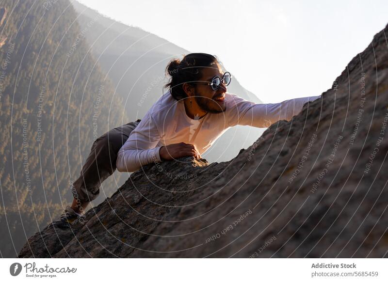 Mutiger junger Mann klettert auf einen Bergfelsen Aufstieg Berge u. Gebirge Kamm positiv Sonnenbrille Stil Klippe Stoff Natur Abenteuer Hochland reisen männlich