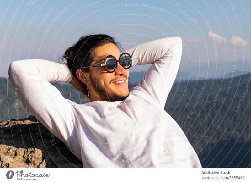 Fröhlicher junger Mann, der sich auf einem felsigen Berg ausruht Berge u. Gebirge Glück Sonnenbrille genießen Natur heiter Zahnfarbenes Lächeln Stil brünett