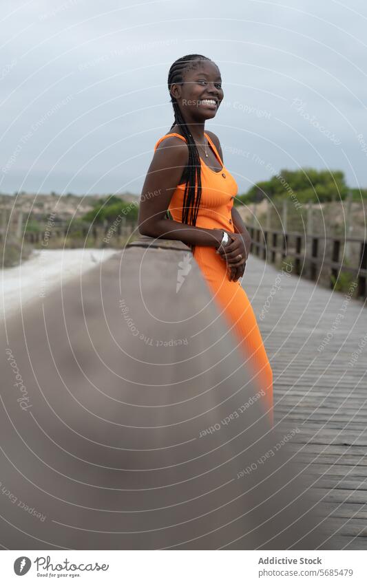 Glückliche afroamerikanische Frau steht auf einer Fußgängerbrücke Brücke Lächeln Promenade Kleid fettarm Geflecht Reling stehen Dame Vorschein positiv