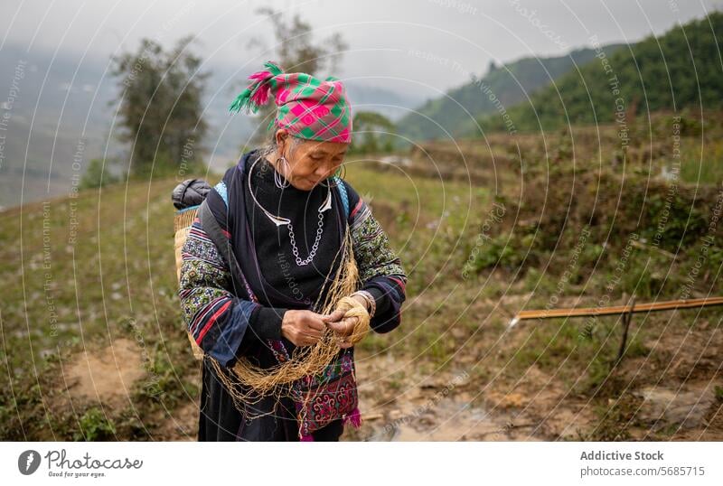 Fokussierte ethnische Frau mittleren Alters mit Faserfaden Konzentration Ackerbau Feld Tradition Landschaft Wasser Pflanze Prozess reif Kopftuch Hobby ländlich