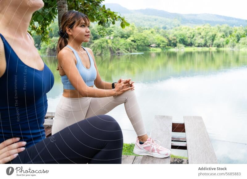 Fröhliche Frauen betrachten die Natur während einer Yoga-Pause Fluss Turnschuh Pier bewundern hölzern Sportkleidung schlank üben Wasser Sportbekleidung stehen