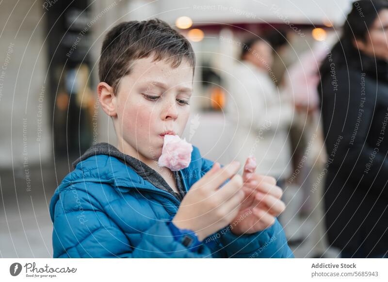 Ein konzentrierter Junge genießt einen Bissen rosa Zuckerwatte in einer geschäftigen städtischen unscharfen Hintergrundeinstellung genießend fokussiert jung