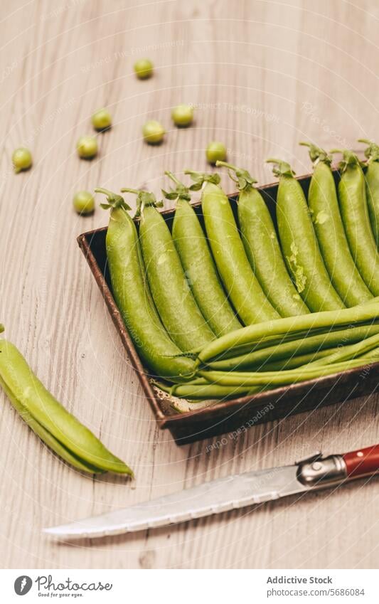 Frische grüne Erbsen in einer rustikalen Schale mit Messer auf Holzunterlage Tablett hölzern Tischplatte reif Gemüse Lebensmittel roh Gesundheit Bestandteil
