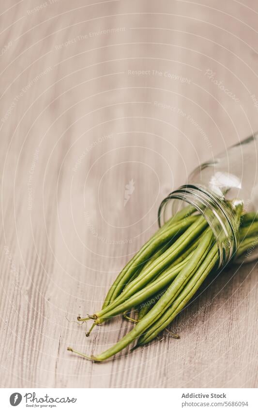 Frische grüne Bohnen, die aus einem Glasgefäß quellen Holzoberfläche frisch Gemüse roh bestückt Kaskadierung Gesundheit Lebensmittel Bestandteil organisch