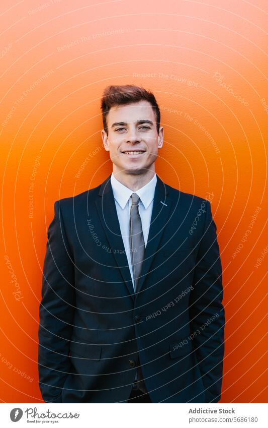 Selbstbewusster Geschäftsmann, der in die Kamera schaut und vor einem orangefarbenen Hintergrund posiert Anzug Lächeln Wand jung männlich professionell