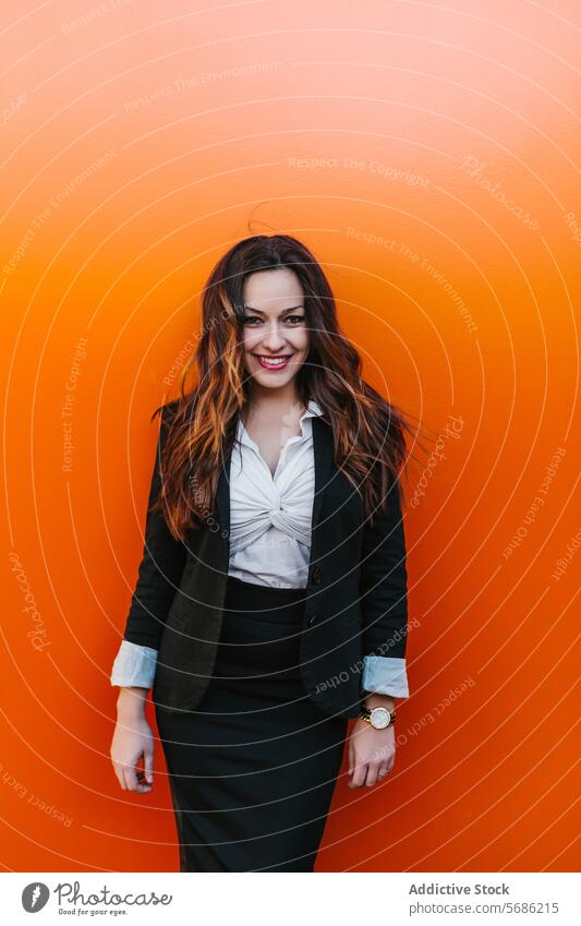 Selbstbewusste Geschäftsfrau mit Blick in die Kamera vor einem orangefarbenen Hintergrund Frau professionell Lächeln selbstbewusst Anzug Madrid Spanien Wand
