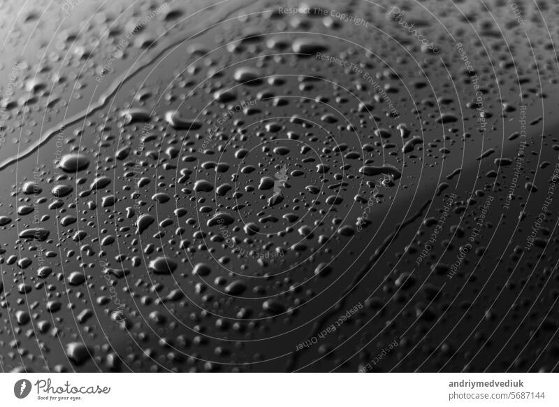 Regen oder Wassertropfen unterschiedlicher Größe auf einem schwarzen glänzenden Auto Motorhaube Oberfläche. Wassertropfen auf dunklem Eisen Oberfläche und Textur. Abstrakter Hintergrund und Wassertextur für Design.