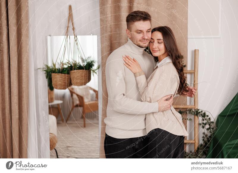 Glückliches junges Paar in der Liebe ist umarmt sanft und lächelnd zusammen feiern Valentinstag in gemütlichen skandinavischen Stil zu Hause. Mann und Frau genießen die Zeit miteinander verbringen, entspannen auf Datum.