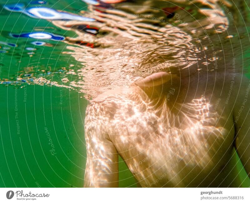 Junge unterwasser, Kopf nicht zu erkennen. Der Oberkörper und die Arme spiegeln sich in der unteren Seite der Wasseroberfläche. Unterwasser See Urlaub Schwimmen