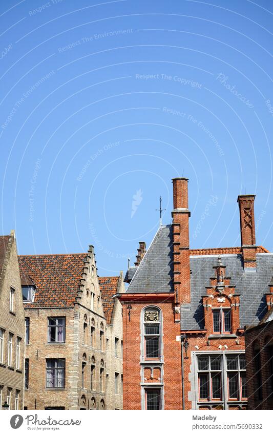 Häuserzeile mit schönem alten Treppengiebelund Backsteinbau in Torbraun mit Schornstein vor blauem Himmel im Sonnenschein in den Gassen der Altstadt von Brügge in Westflandern in Belgien