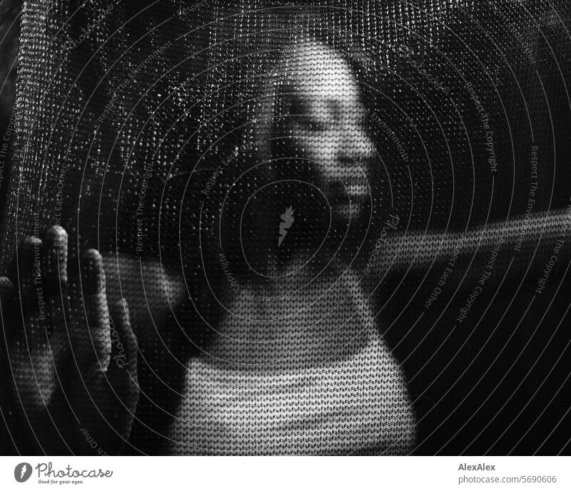 Junge, langhaarige Frau stützt sich hinter transparentem Vorhang/Netz im Halbdunkel ab junge Frau schwarz schwarzweiß Transparenz Erwachsene durchsichtig
