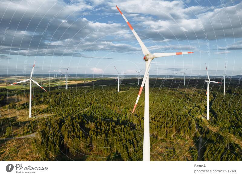 Windkraftanlagen in einem hügeligen Wald vor einem teilweise bewölkten, aber sonnigen Himmel aus der Vogelperspektive bei Sonnenuntergang Antenne Sauberkeit