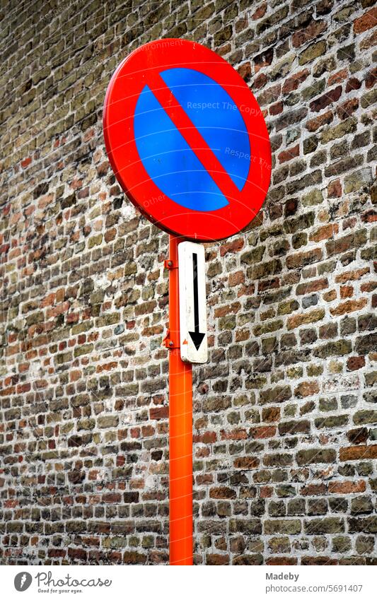 Halteverbot Verkehrszeichen mit Pfeil in Rot und Orange vor einer alten Mauer und Fassade aus Backstein in den Gassen der Altstadt von Brügge in Westflandern in Belgien