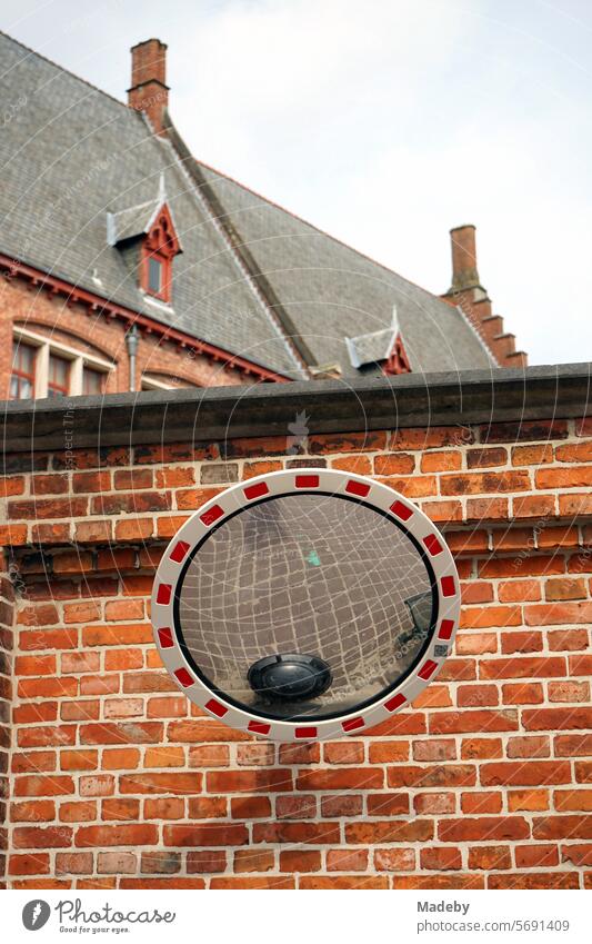Runder Verkehrsspiegel mit Spiegelung des Straßenpflaster vor einer Backsteinmauer in Rotbraun einer alten Schule in den Gassen der Altstadt von Brügge in Westflandern in Belgien